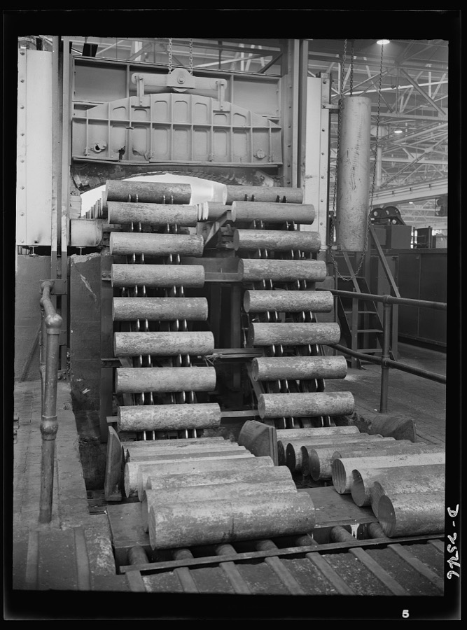Conversion. Copper and brass processing. A mechanical feeder is here shown running billets of brass into an electric furnace, where they will be heated at a high temperature. Then the heated billets will be pushed with tremendous force through the die of an extrusion machine to form rods, tubes, angles or other shapes. Chase Brass and Copper Company, Euclid, Ohio