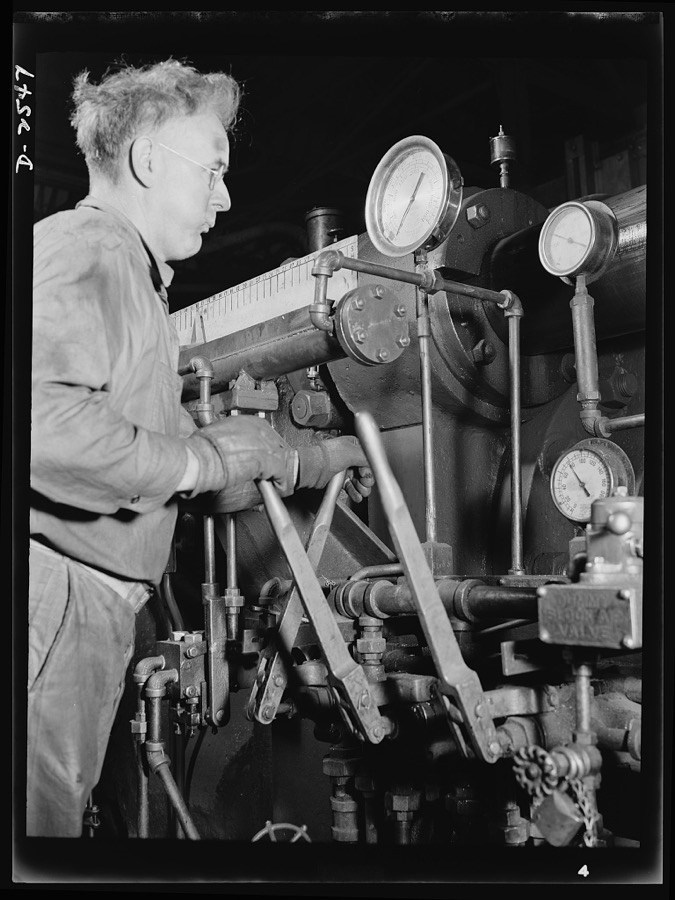 Conversion. Copper and brass processing. This worker is at the controls of an extruding machine, a powerful piece of apparatus in a brass and copper mill that pushes billets of metal usually heated red hot, through a die to form rods, tubes, angles, channels and other shapes. Chase Brass and Copper Company, Euclid, Ohio