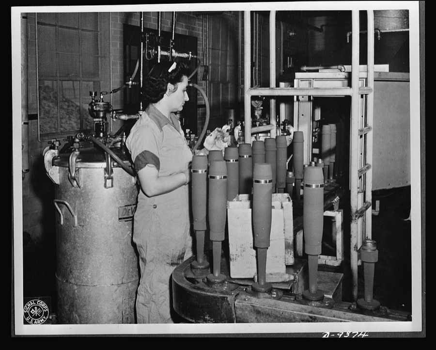 Production. Shell loading. On the "firing line" of a large Midwest loading plant, artillery shells soon to batter the Axis are sprayed with olive drab paint. This women is a sprayer, but women also do the "puddling" of TNT in shells better than men. For "puddling," the stirring and packing of TNT in shells, is done much as a housewife prepares dough for cake. Ravenna ordnance plant