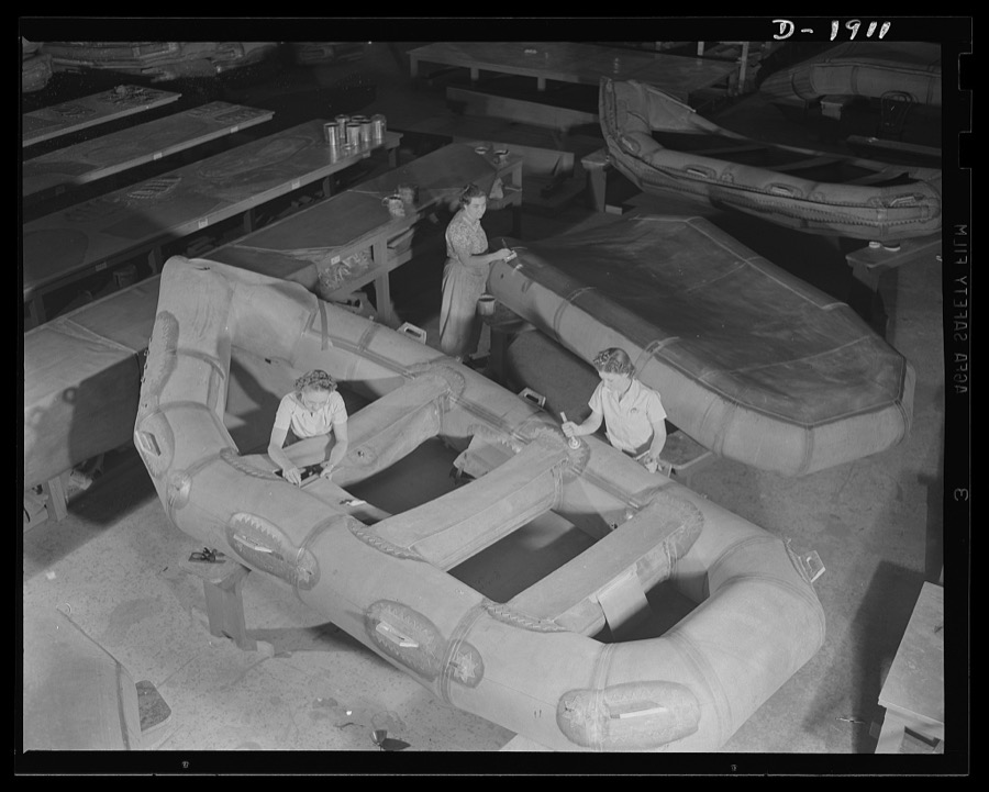 Assault boat Production. Building assault boats for U.S. Marine Corps. Women workers in balloon room. In foreground they are applying seats and accessories to boat while worker in background is applying coat of rubber paint to bottom of boat. Goodyear, Akron, Ohio