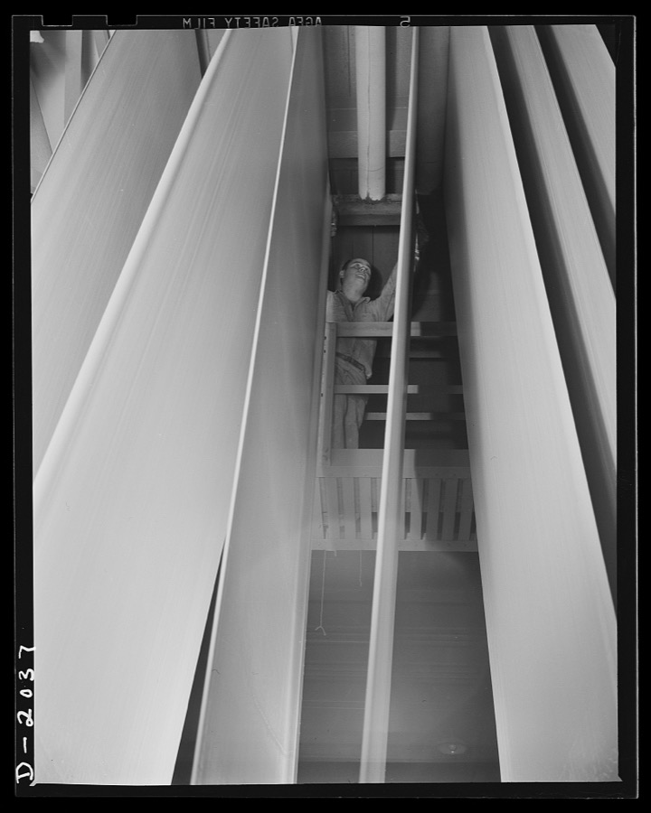 Drying at top speed. Reeled away from the calendaring machine, the fresh stock rolls over towering drying racks shown here. Weighted tension bars keep the festooned sheet of new fabric taut and straight as it cools and dries. From the drying racks, the fabric travels quickly onto rolls of cloth where it is rolled onto reels small enough to handle. Firestone (General Tires), Akron, Ohio